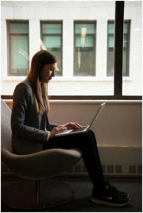 Woman sitting on a chair using a laptop by the win