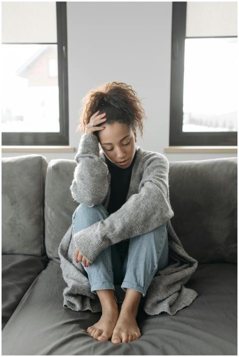 A woman in cozy attire sits on a sofa indoors, app