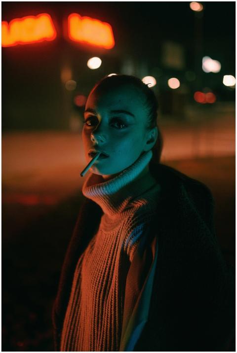 A woman smokes a cigarette at night in a city, bat