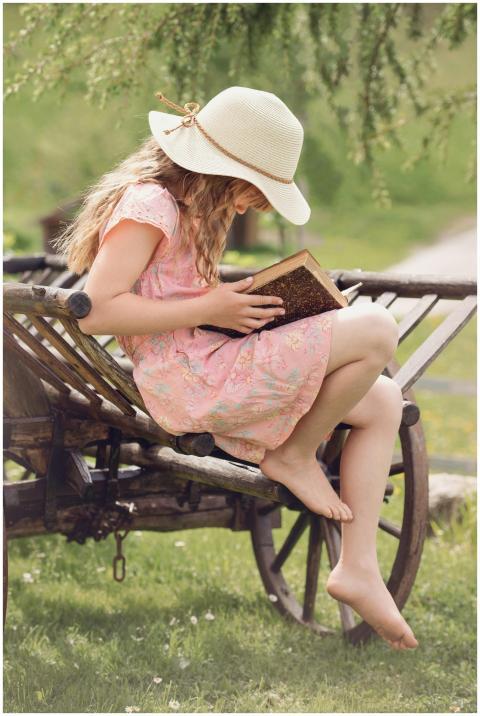 A young girl in a hat reads a book while sitting o