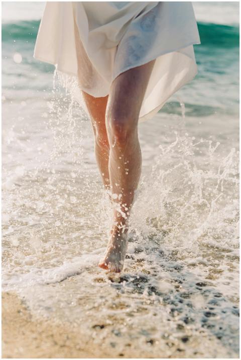 A woman walks barefoot along the beach with water