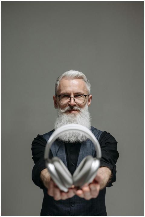 Senior man with beard presenting headphones in a s