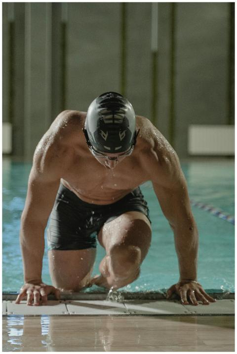 A muscular male swimmer stepping out of an indoor