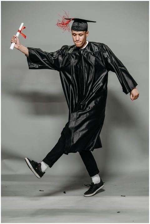 Happy graduate in cap and gown joyfully dancing wi