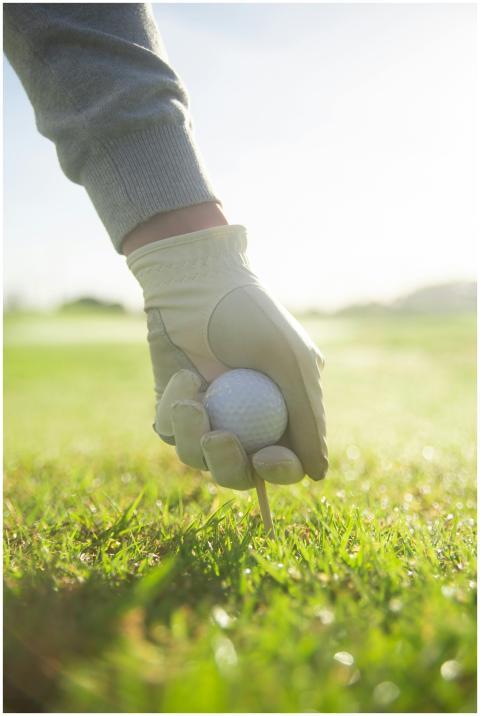 A gloved hand setting a golf ball on a tee in a su