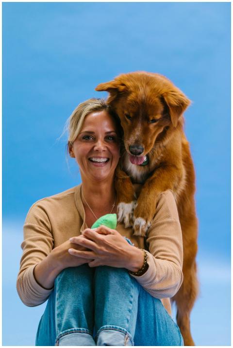 A cheerful woman sits with her brown dog in a cozy