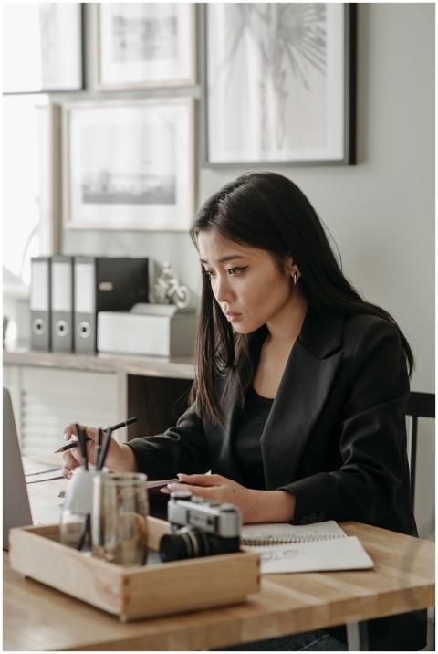 Asian woman in blazer taking notes during an onlin