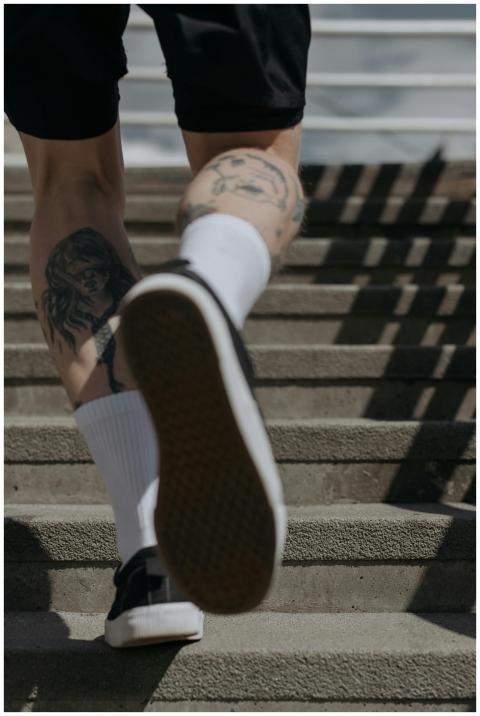 Close-up of tattooed legs in black sneakers climbi