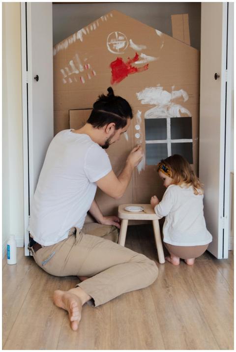 Father and daughter painting a cardboard house ind