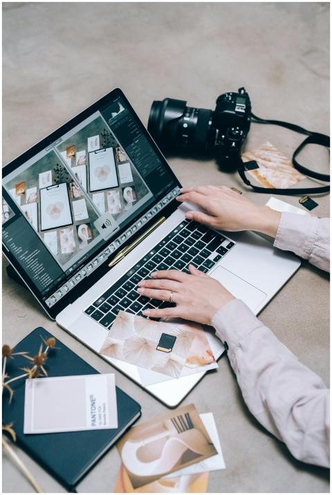 Hands editing photos on a laptop with a camera nea