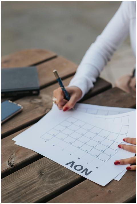 A woman writes on a November calendar outdoors, pl