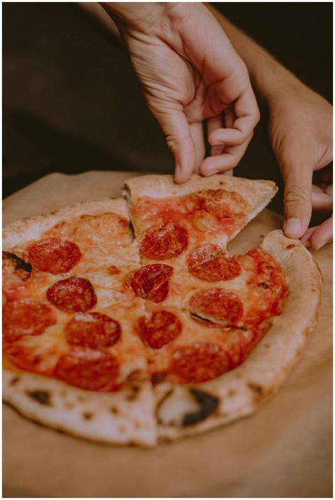 Close-up of hands serving a cheesy pepperoni pizza