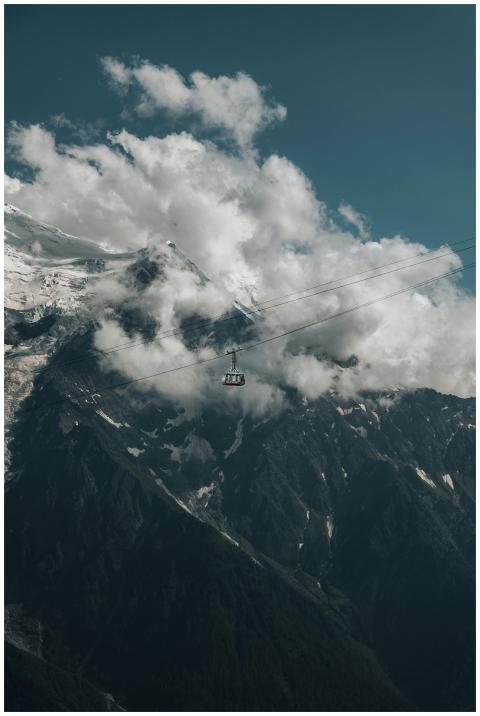 Suspended cable car amidst cloudy mountain peaks,