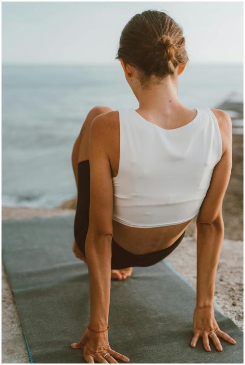 Woman practicing yoga on a mat by the ocean at sun