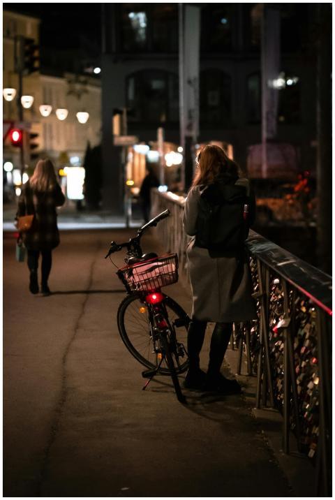 A woman stands with her bicycle on a dimly lit cit