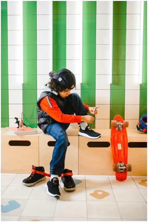 A young boy in a snapback hat ties his shoes while