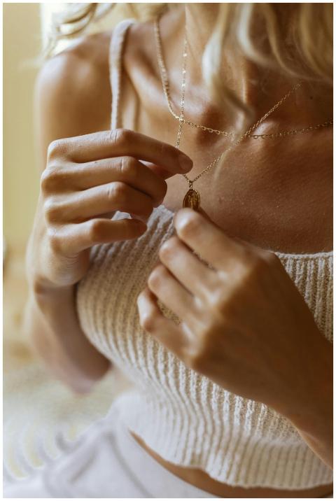 A woman adjusts her delicate gold necklace, wearin