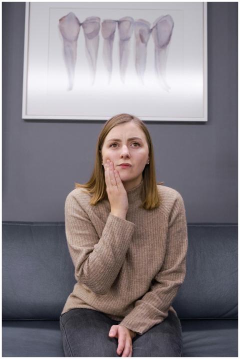 Woman in a brown sweater holding her cheek, indica