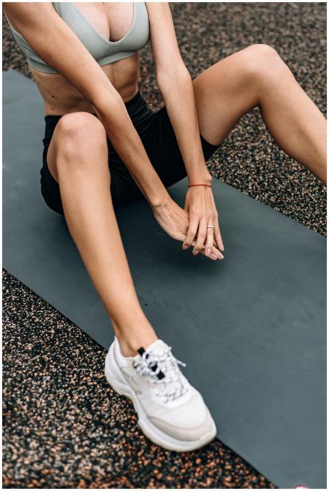 Fit woman stretching on mat outdoors, embracing he