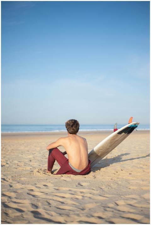 A shirtless surfer sits on a sandy beach in Portug