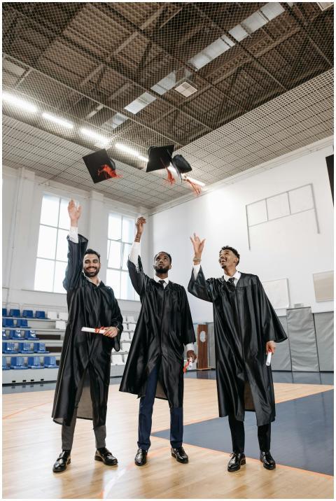 Three male graduates in gowns celebrate with cap t