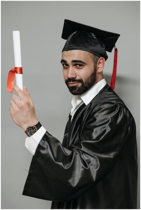 A bearded man in graduation attire proudly holding