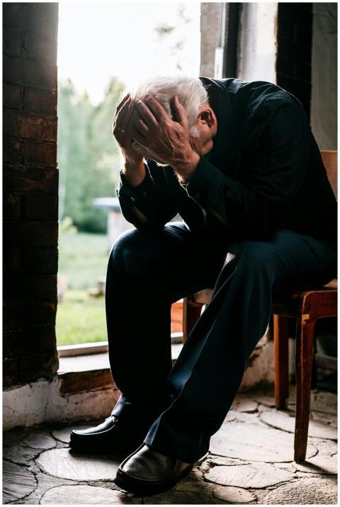 Senior man in black, grieving alone, sitting on a