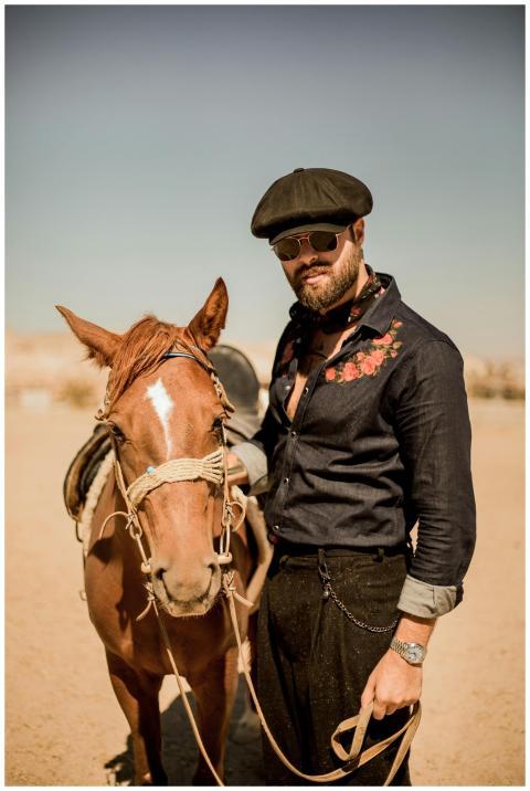 A stylish man stands beside a horse in Ortahisar,