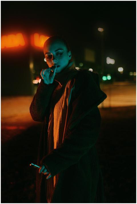A woman smokes a cigarette on a city street at nig