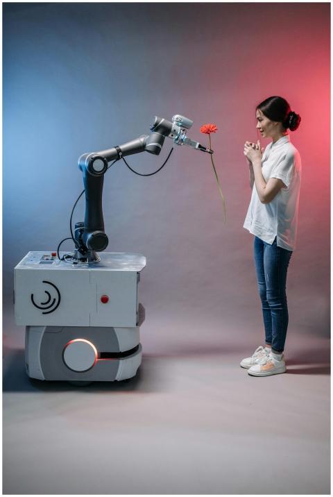 A robot arm presents a flower to a smiling woman,