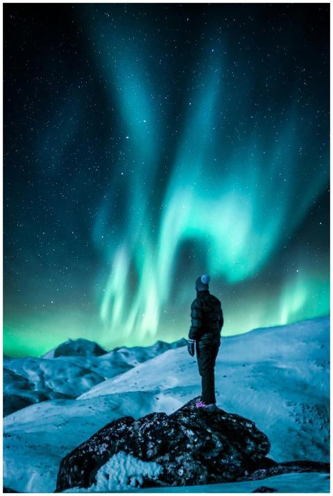 A lone figure stands on a snowy slope, gazing at t