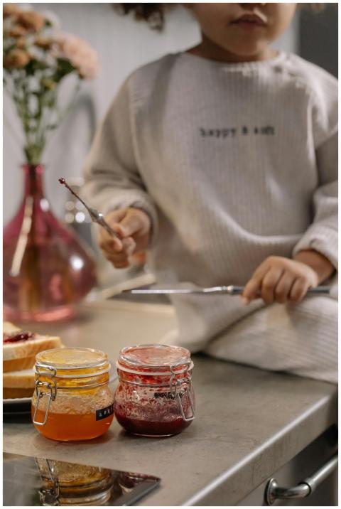 Cute child with jars of fruit jams enjoying breakf