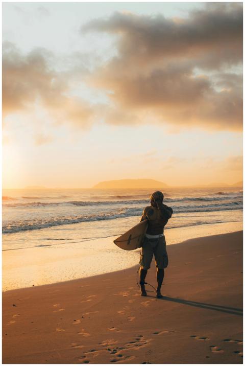A surfer holding a board walks along a sandy beach