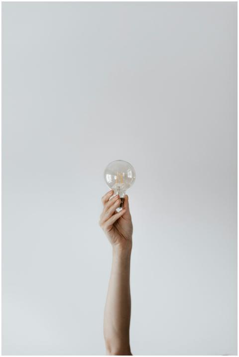 A hand raises a light bulb against a soft gray bac