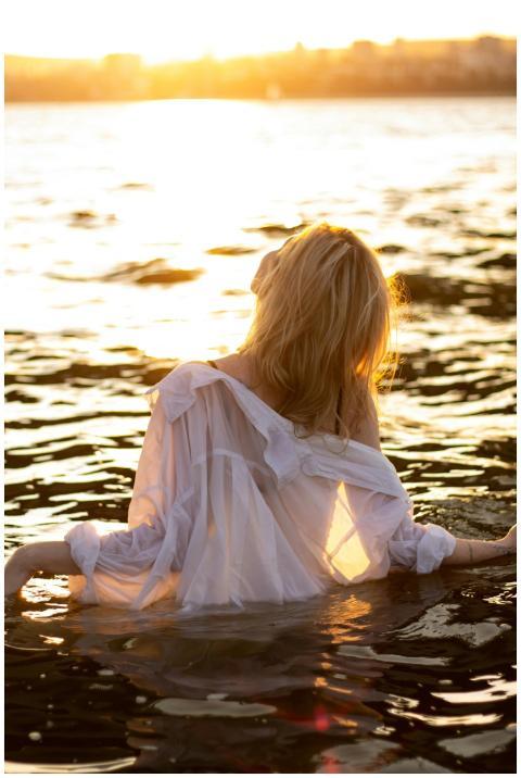 A woman in a white dress stands in water at sunset