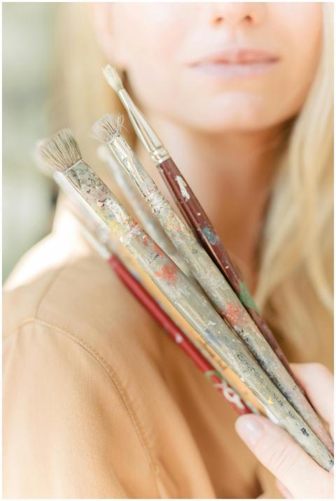 A blurred close-up of a woman holding paintbrushes