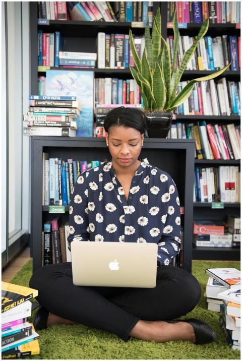 Woman sitting on carpet with laptop, surrounded by