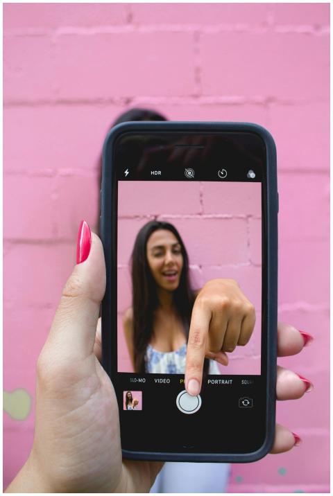 A woman captures her selfie using a smartphone aga