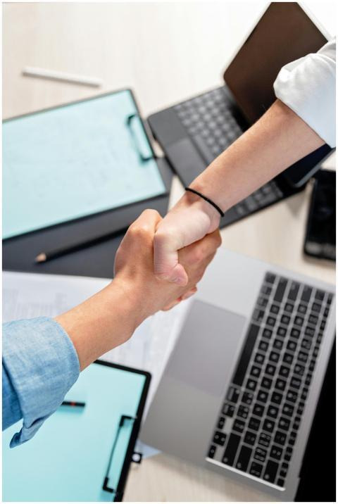Two people shaking hands over laptops and document