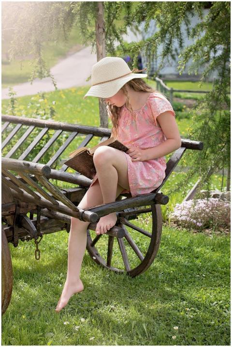 A young girl in a sun hat reads a book while sitti