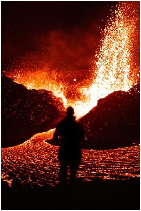 A silhouette stands before a vibrant eruption, sho