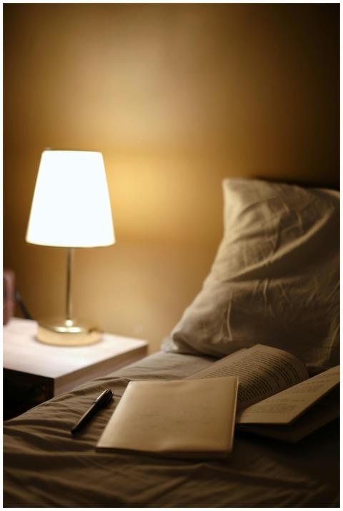 Warm bedside scene with open books, lamp, and a pi