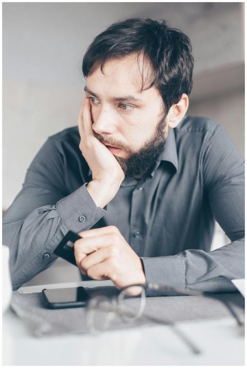 A worried man in a gray shirt holds a credit card,
