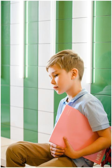 Young boy sitting indoors, holding a pink book, wi
