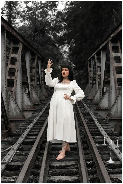 A woman in a vintage white dress poses on old rail