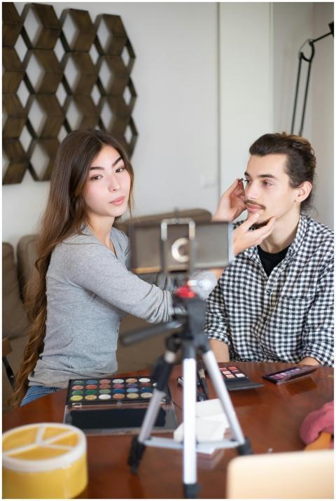 Asian woman applies makeup to a Caucasian man for