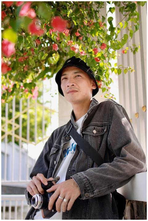Man with camera in denim jacket under flowering tr