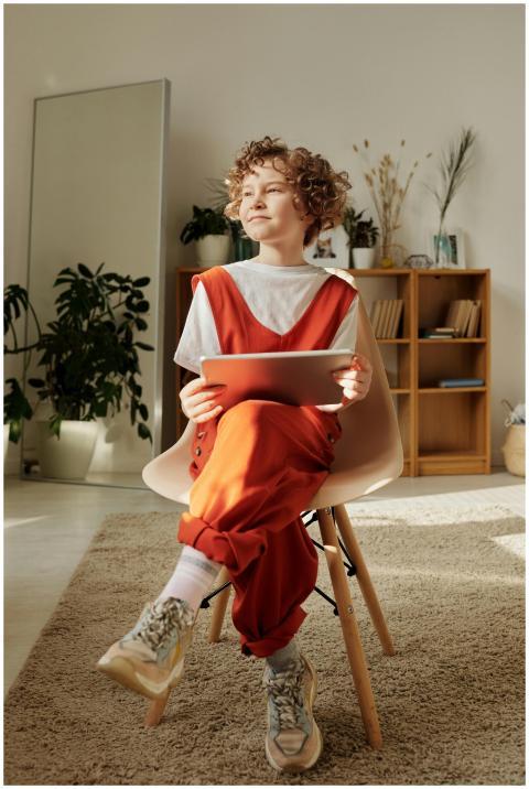 A cheerful child sits indoors, using a tablet for