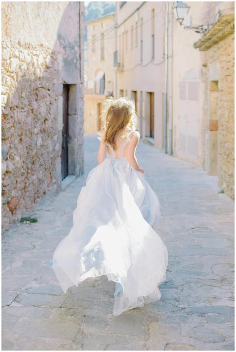 A woman in a dreamy, flowing dress runs down a nar