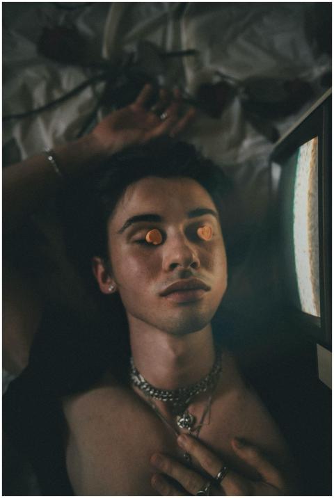 A young adult with pills on closed eyes, lying nea